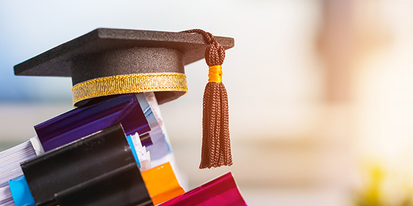 Image of a graduation cap sitting on top of a stack of books on a table.
